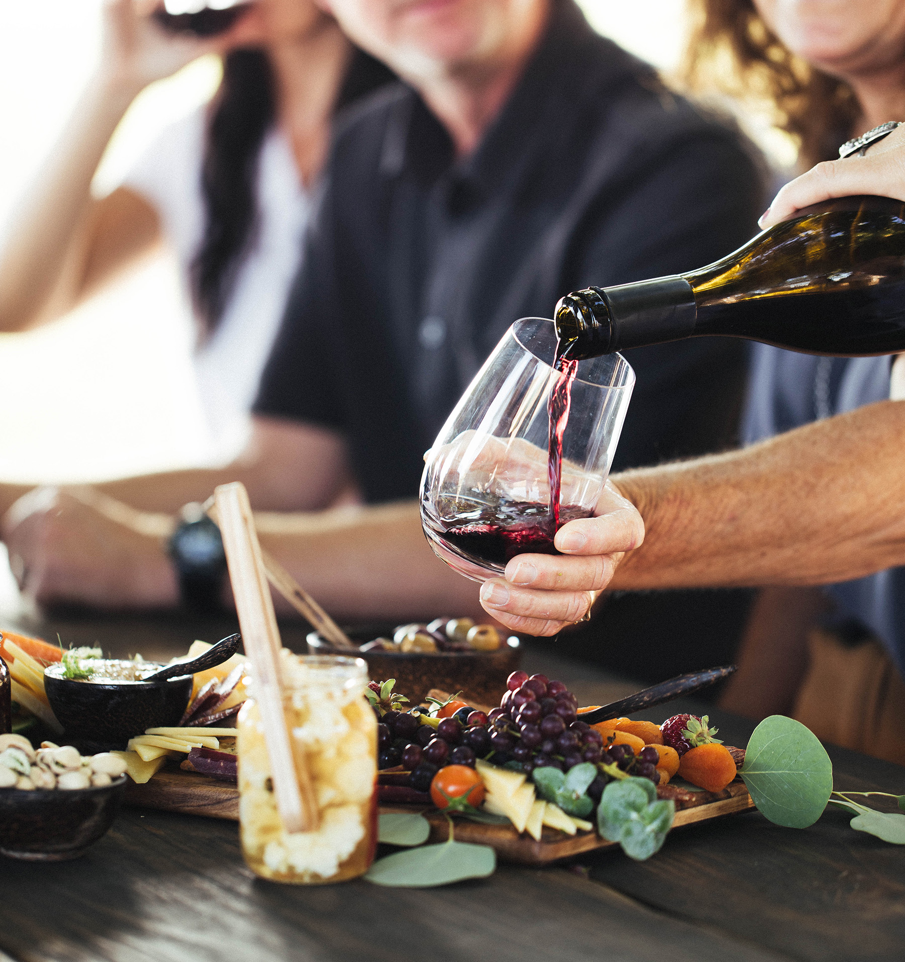 Baileyana Pinot Noir being poured into glass against a cheese and charcuterie board backdrop